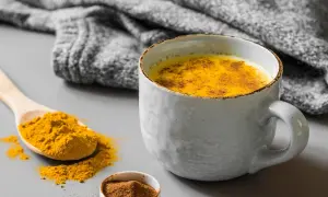 Un latte dorato speziato, perfetto cosa bere al posto del caffè. Curcuma e cannella in una tazza calda, con una coperta grigia sullo sfondo.