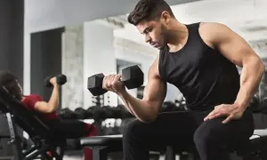 Uomo concentrato esegue esercizi con manubri in palestra. A sinistra, una donna fa lo stesso su una panca inclinata.