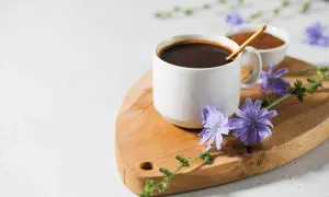 Tazza di caffè di cicoria scuro su tagliere di legno, decorata con fiori di cicoria viola.