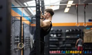 Uomo concentrato esegue trazioni alla sbarra in palestra, allenando la schiena e le braccia.