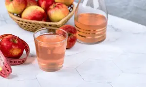 Un bicchiere di aceto di mele, mele fresche in un cesto e una bottiglia decorata. Un metro da sarta rosa avvolge una mela, suggerendo un percorso di benessere.