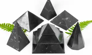 Piramidi di shungite elite, note per le loro proprietà uniche, disposte su sfondo bianco con foglie verdi.