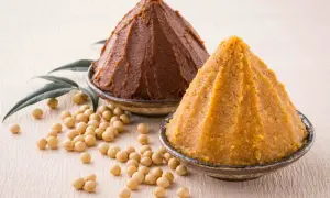 Due ciotole con miso, uno scuro e uno chiaro, circondate da fagioli di soia. Il miso è una pasta fermentata giapponese.