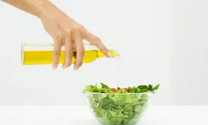 Mano versa olio su un'insalata fresca, un passo per un'insalata per dimagrire gustosa e salutare.