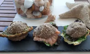 Tre panini low carb ricetta: uno con pesto, uno con salmone affumicato e insalata, uno con formaggio e insalata. Decorazioni marine sullo sfondo.