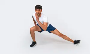 Uomo in posizione di affondo laterale, parte di una serie di 12 esercizi a corpo libero per allenarsi a casa.