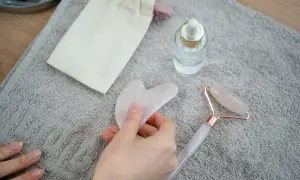 Mano che tiene una pietra gua sha rosa, accanto a un rullo di quarzo e un siero. Utile per il benessere, ma attenzione alle gua sha controindicazioni.