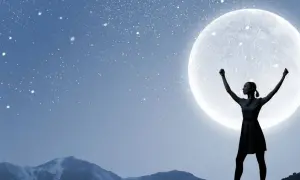 Silhouette di una donna con le braccia alzate, che sembra chiedere un desiderio alla luna piena, sotto un cielo stellato e montagne innevate.
