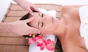 Un massaggio per mal di testa rilassante, con mani esperte che accarezzano la fronte e le tempie. Fiori rosa aggiungono un tocco di serenità.