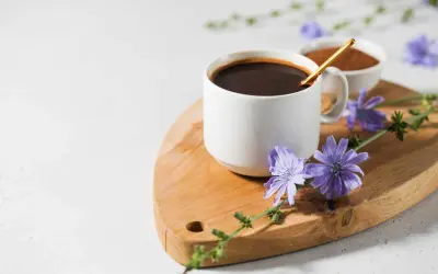 Tazza di caffè di cicoria scuro su tagliere di legno, decorata con fiori di cicoria viola.
