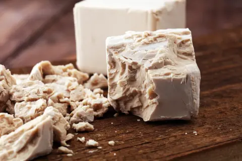 Blocchi di lievito di birra fresco, alcuni sbriciolati, pronti per essere usati. Scopri come assumere il lievito di birra per i tuoi impasti.