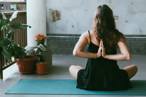 Donna in posizione yoga, mani giunte dietro la schiena, per alleviare i **secondo chakra bloccato sintomi**.