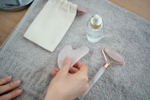 Mano che tiene una pietra gua sha rosa, accanto a un rullo di quarzo e un siero. Utile per il benessere, ma attenzione alle gua sha controindicazioni.