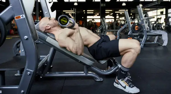 Uomo calvo esegue panca inclinata con bilanciere, uno dei fondamentali esercizi palestra per la parte alta del corpo.