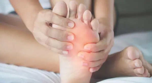 Mani che massaggiano un piede, evidenziando il dolore sotto le dita. Si cercano rimedi naturali per alleviare il fastidio.