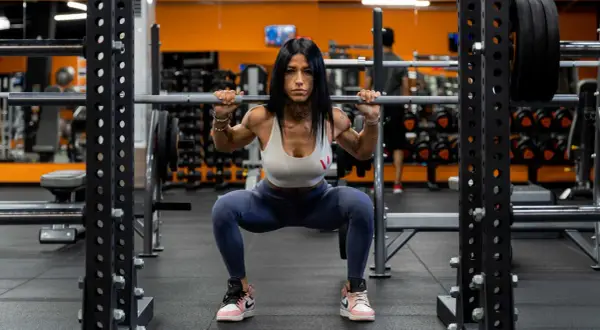 Donna in palestra esegue uno squat con bilanciere, dimostrando come fare bene gli squat con tecnica e concentrazione.