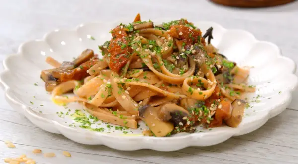 Pasta integrale con funghi e pomodori secchi, un'idea per le tue cucina macrobiotica ricette. Guarnita con semi di sesamo e prezzemolo.