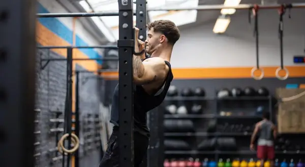Uomo concentrato esegue trazioni alla sbarra in palestra, allenando la schiena e le braccia.