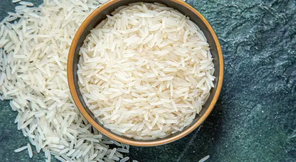 Chicchi di riso basmati in una ciotola e sparsi su una superficie scura. Scopri le proprietà del riso basmati.