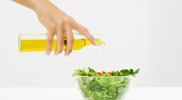 Mano versa olio su un'insalata fresca, un passo per un'insalata per dimagrire gustosa e salutare.