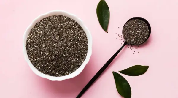 Semi di chia in una ciotola e un cucchiaio, con foglie verdi. Un aiuto naturale per la menopausa.