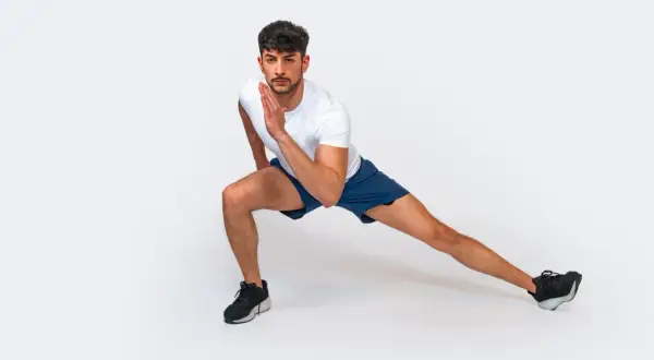 Uomo in posizione di affondo laterale, parte di una serie di 12 esercizi a corpo libero per allenarsi a casa.