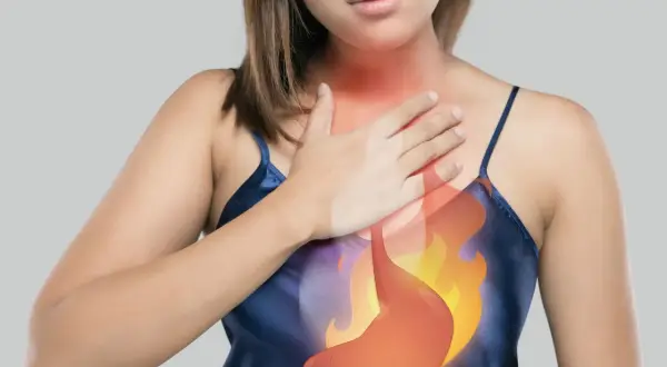 Donna con mano sul petto, immagine dello stomaco in fiamme. Potrebbe indicare bruciore o ernia iatale, suggerendo un possibile automassaggio.