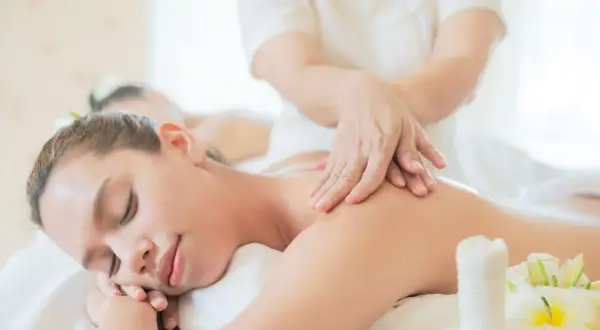 Mani esperte mostrano come fare un massaggio alla schiena rilassante, con fiori di plumeria e un sacchetto di erbe.