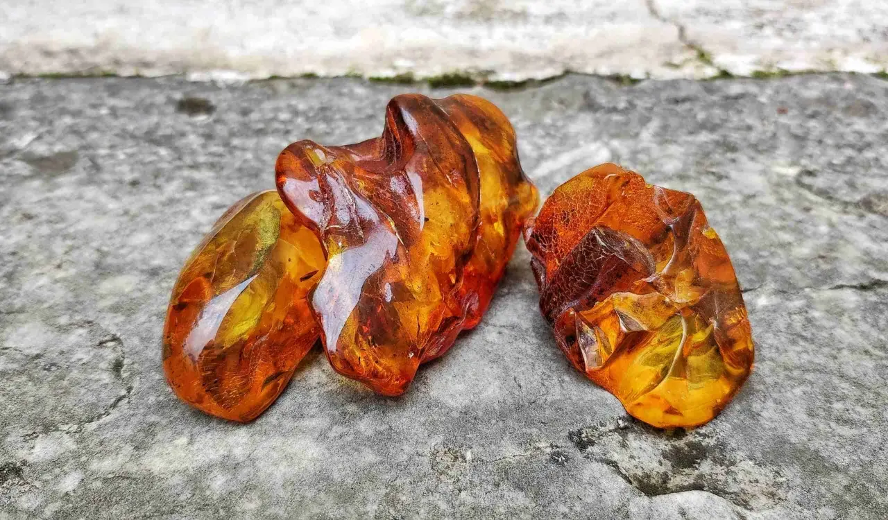 Tre pezzi di ambra baltica grezza, luminosi e traslucidi, mostrano le loro affascinanti proprietà naturali su una superficie rocciosa.