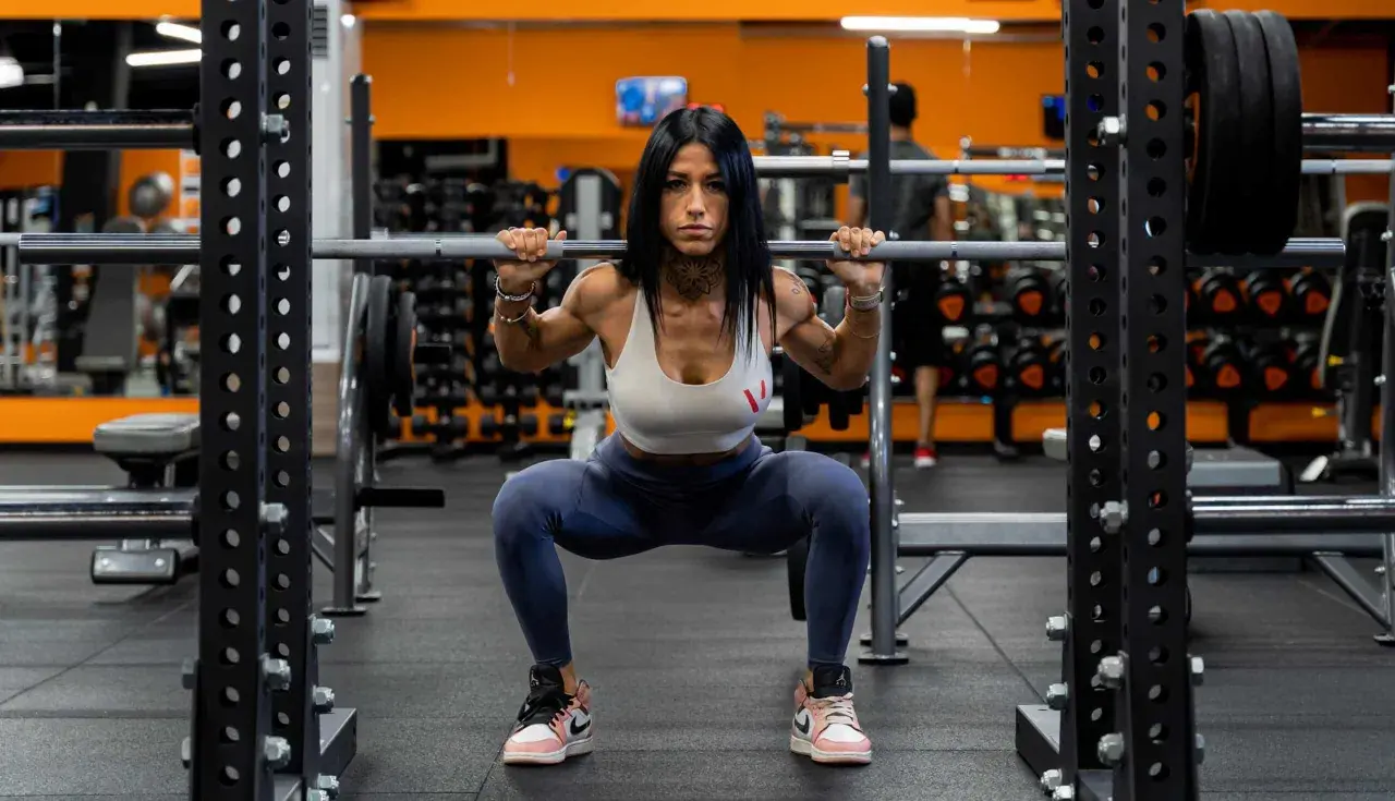 Donna in palestra esegue uno squat con bilanciere, dimostrando come fare bene gli squat con tecnica e concentrazione.