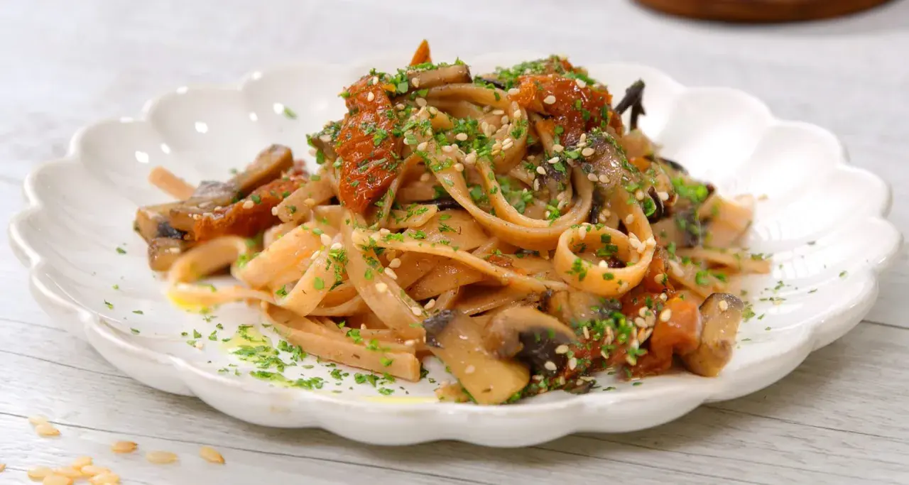 Pasta integrale con funghi e pomodori secchi, un'idea per le tue cucina macrobiotica ricette. Guarnita con semi di sesamo e prezzemolo.