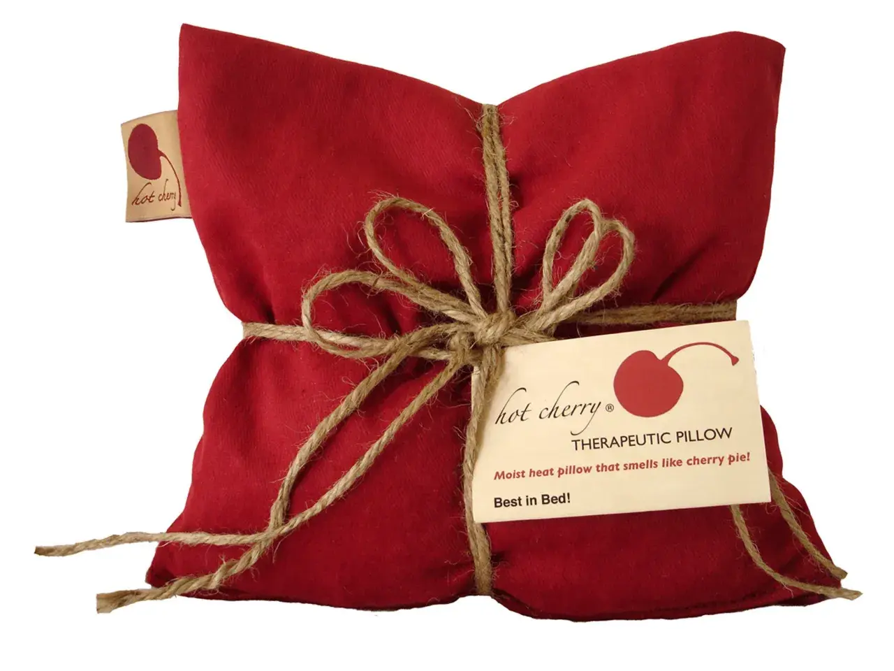 Cuscino rosso con noccioli di ciliegia, legato con spago. Un'etichetta recita "Hot Cherry Therapeutic Pillow". Benefici rilassanti.