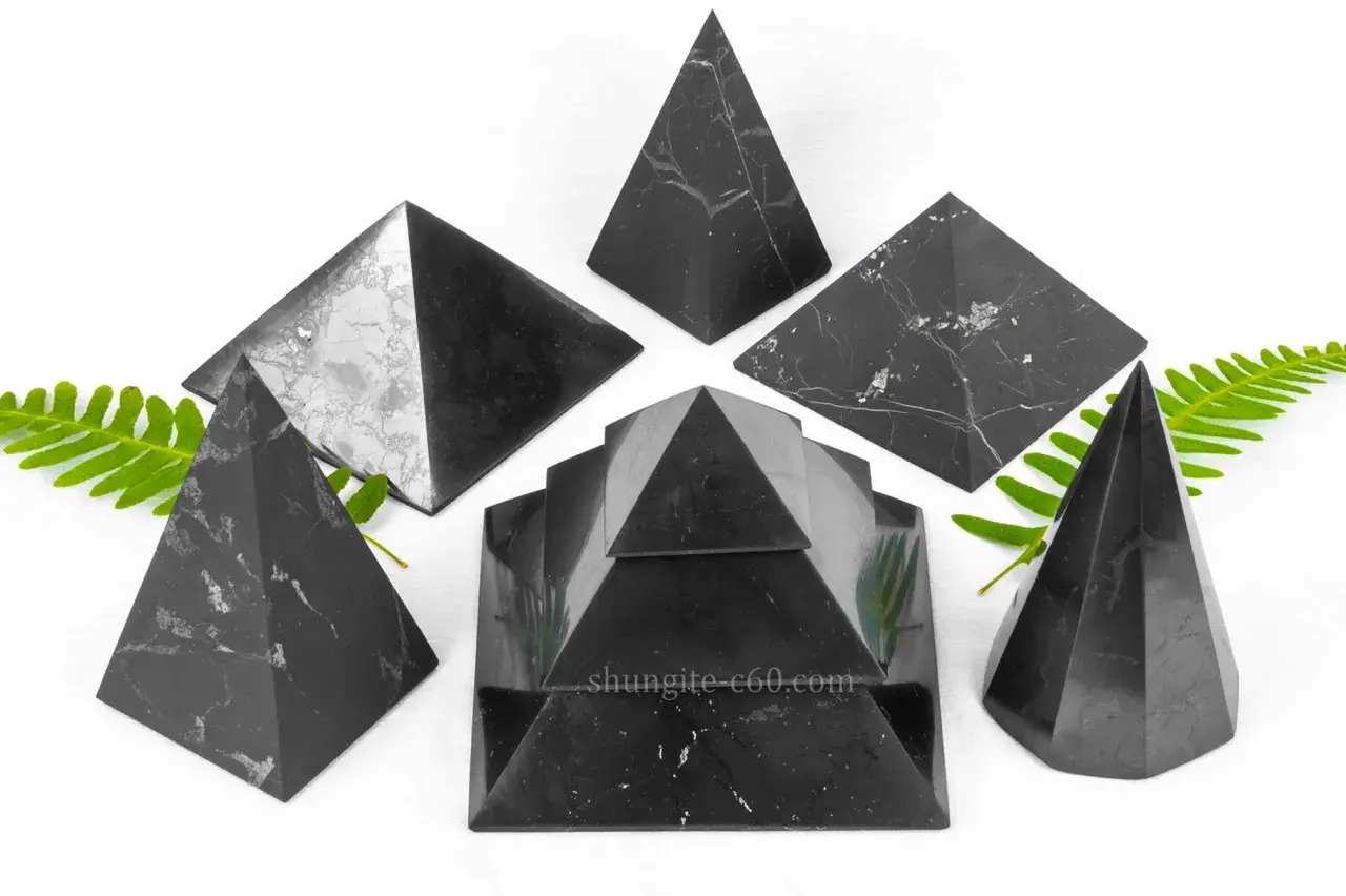 Piramidi di shungite elite, note per le loro proprietà uniche, disposte su sfondo bianco con foglie verdi.