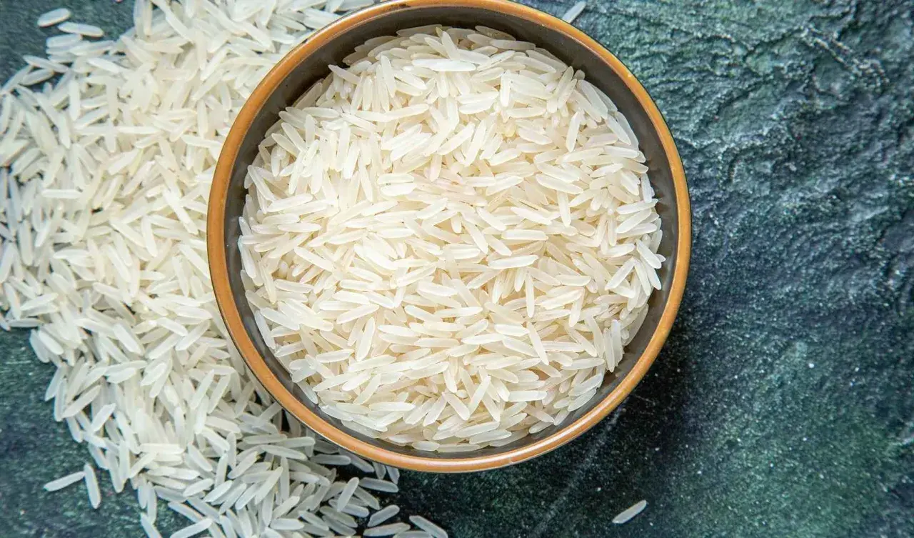 Chicchi di riso basmati in una ciotola e sparsi su una superficie scura. Scopri le proprietà del riso basmati.