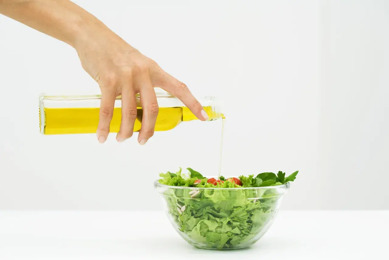 Mano versa olio su un'insalata fresca, un passo per un'insalata per dimagrire gustosa e salutare.