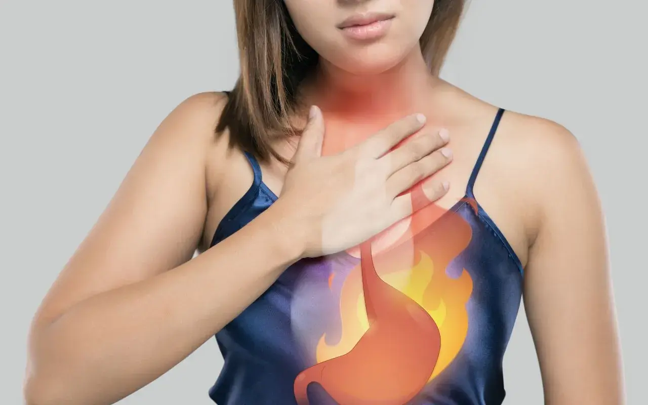 Donna con mano sul petto, immagine dello stomaco in fiamme. Potrebbe indicare bruciore o ernia iatale, suggerendo un possibile automassaggio.