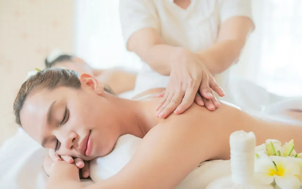 Mani esperte mostrano come fare un massaggio alla schiena rilassante, con fiori di plumeria e un sacchetto di erbe.