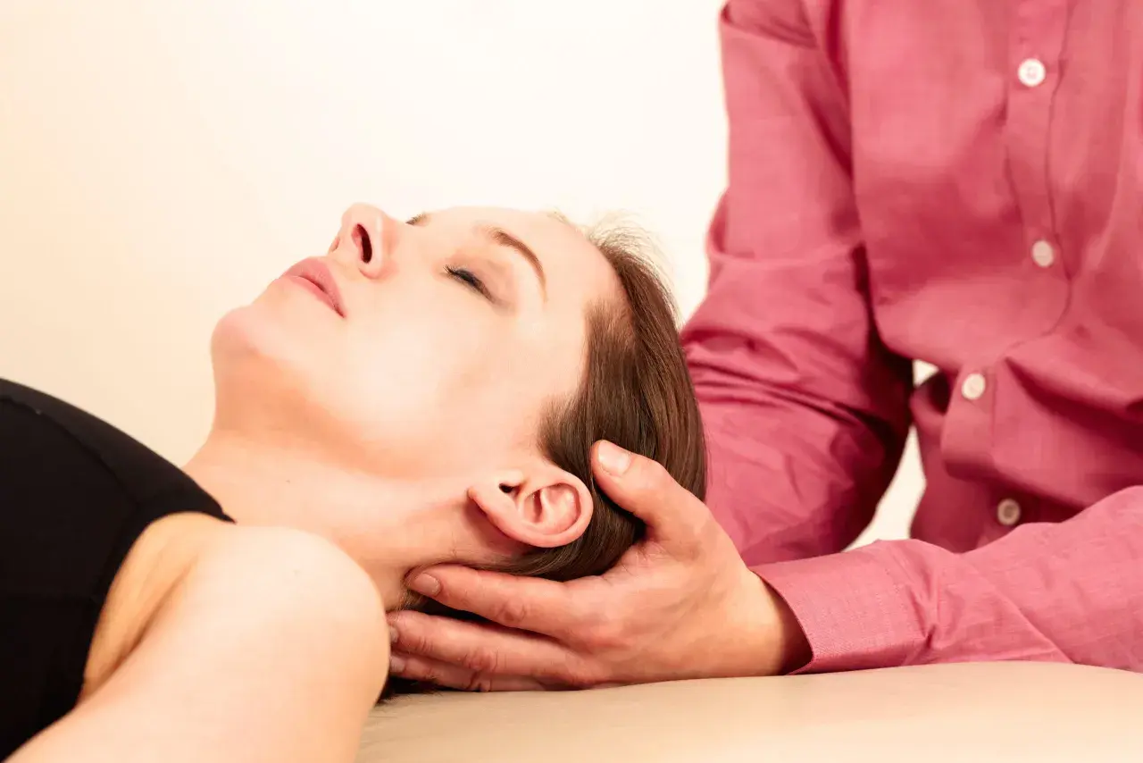 Mani che sostengono delicatamente la testa di una donna, suggerendo i benefici del cranio sacrale per il rilassamento e il benessere.