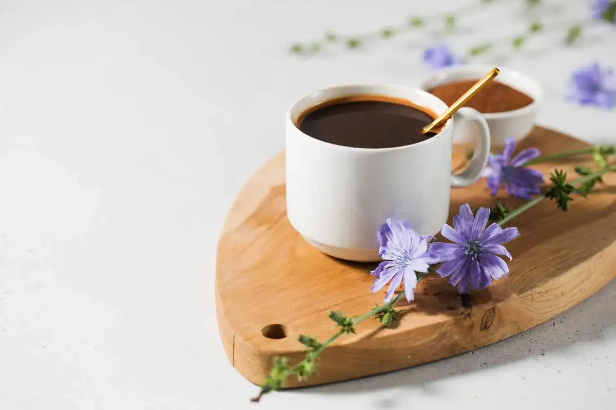 Tazza di caffè di cicoria scuro su tagliere di legno, decorata con fiori di cicoria viola.