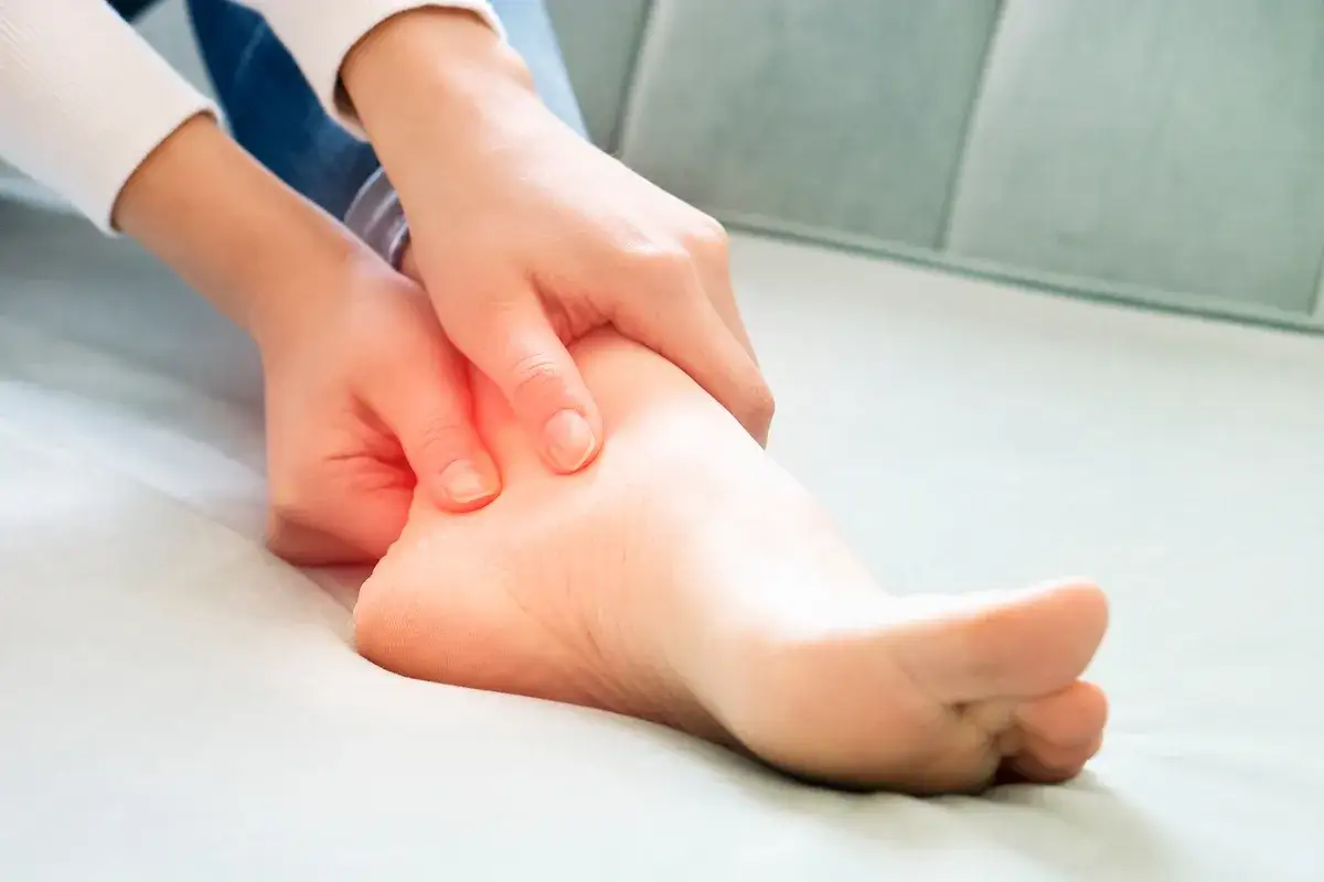 Mani che massaggiano un piede dolente, con un'area rossa che indica il dolore. Potrebbe essere utile per capire cos'&egrave; il drenaggio linfatico.