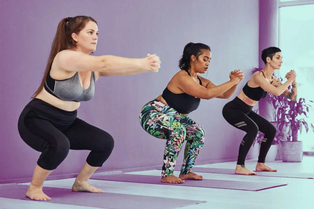 Tre donne praticano squat su tappetini viola, imparando come fare bene gli squat.