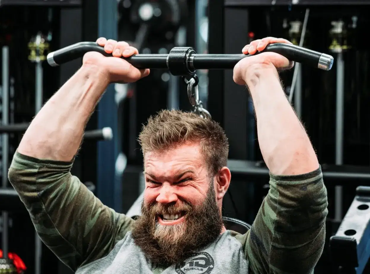 Uomo con barba esegue esercizi tricipiti macchinari con sforzo visibile, concentrato sul movimento.