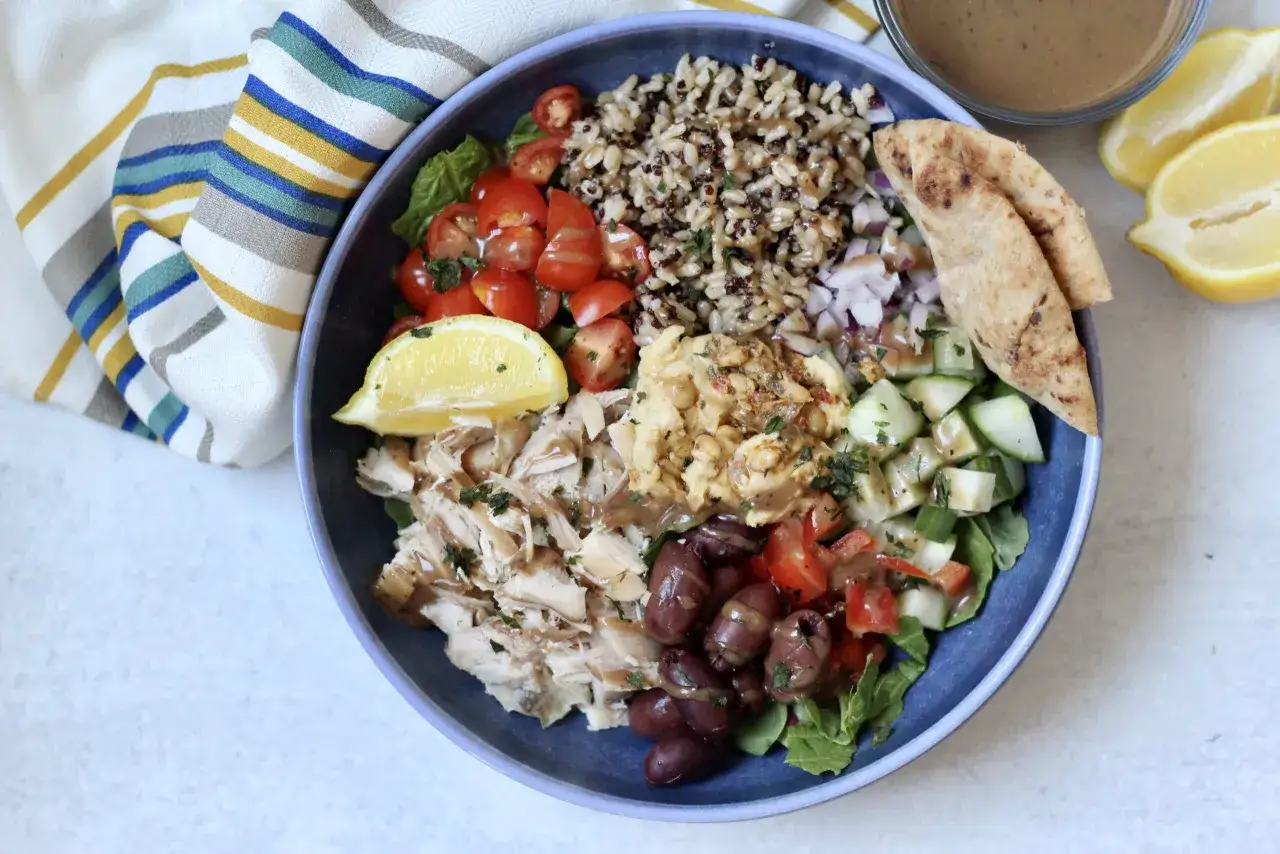 Insalata colorata con pollo sfilacciato, verdure fresche, olive, hummus e un mix di cereali integrali, ricca di carboidrati non raffinati.