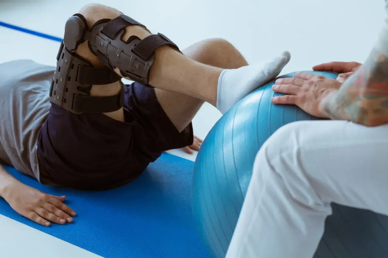 Paziente con tutore al ginocchio esegue esercizi con palla da fisioterapia. Quanto camminare dopo protesi ginocchio? La riabilitazione è fondamentale.