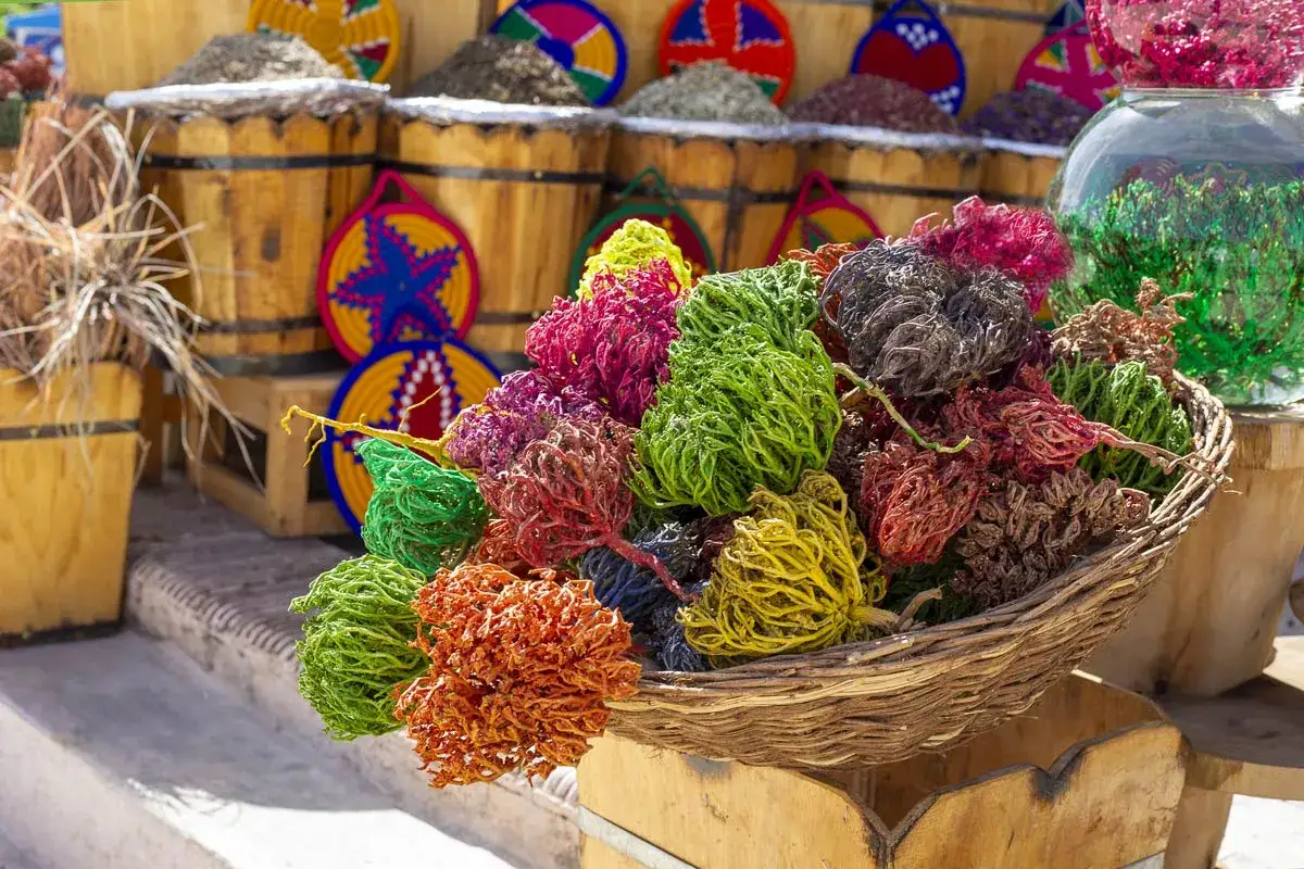 Cesto pieno di colorate rose di Gerico, un simbolo di rinascita, accanto a barili di spezie e decorazioni artigianali.