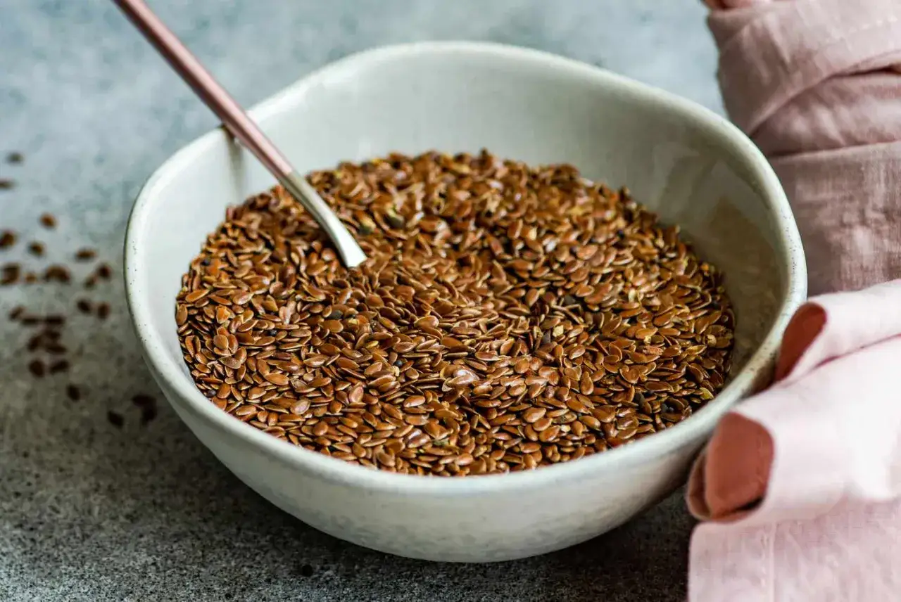 Una ciotola piena di semi di lino marroni, pronti per essere mangiati crudi. Un cucchiaio rosa &egrave; immerso nei semi.
