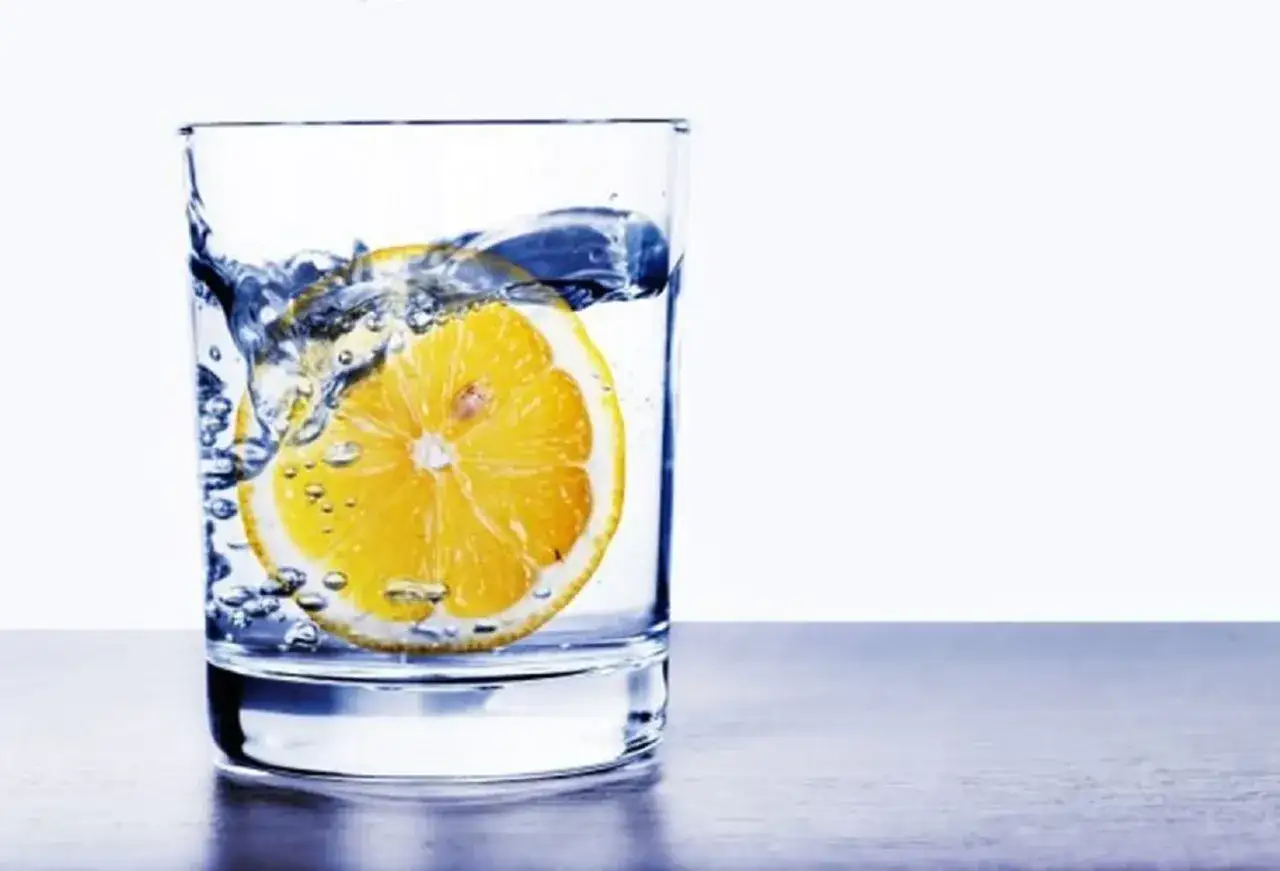 Un bicchiere di acqua e limone, con una fetta di limone che galleggia e crea bollicine. Un'immagine fresca e dissetante.