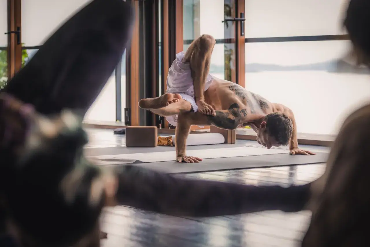 Uomo in posa yoga avanzata, corpo tatuato, equilibrio perfetto. Un'espressione di energia maschile e femminile in armonia.