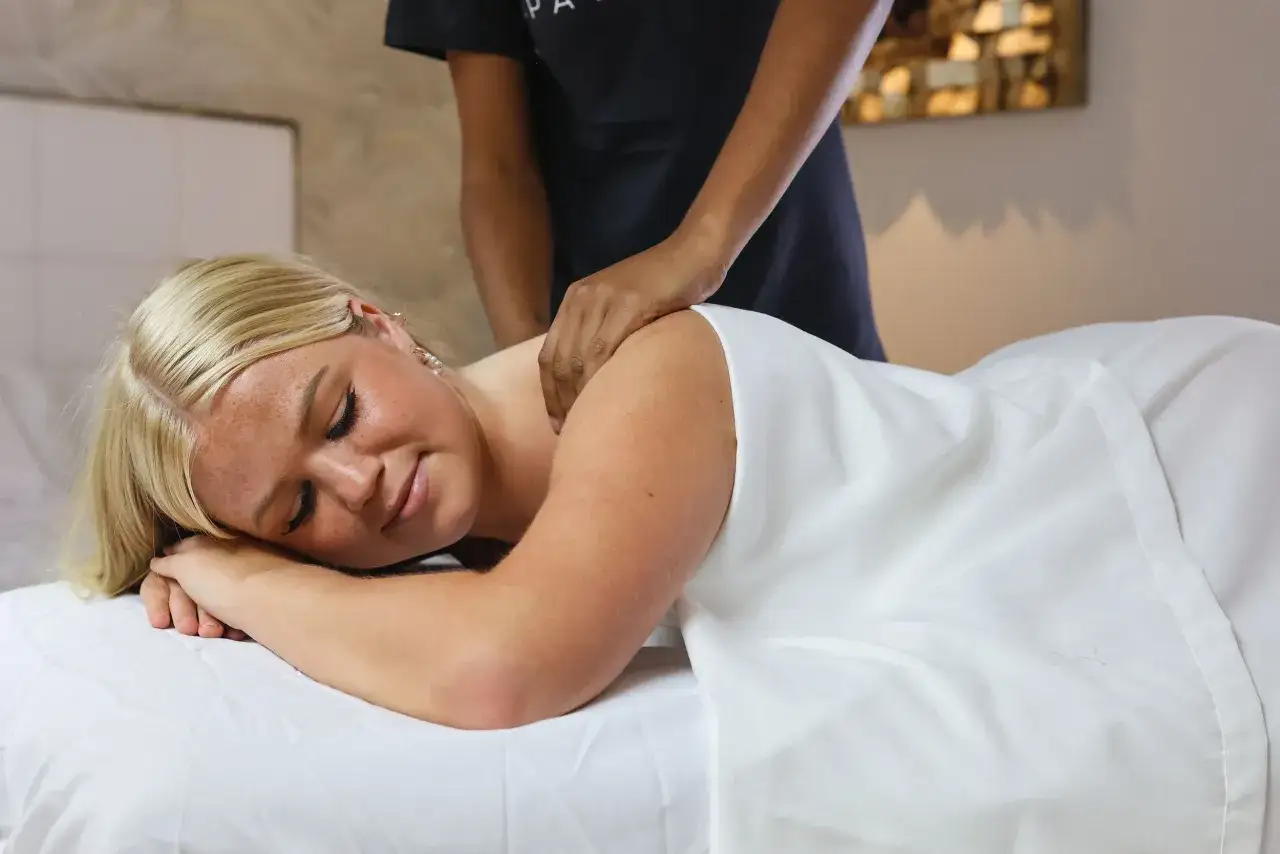 Donna bionda riceve un massaggio rilassante tutto il corpo, con gli occhi chiusi e un'espressione serena.