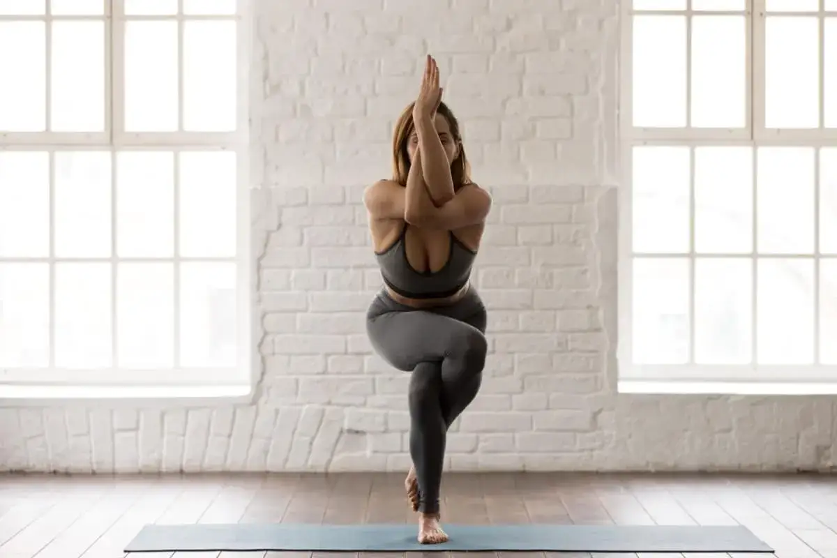 Donna in posa yoga Garudasana, un esercizio che richiede equilibrio e concentrazione, principi fondamentali degli yama e niyama.
